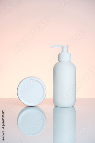 Hand cream in a bottle and jar on a light pink background with reflection.