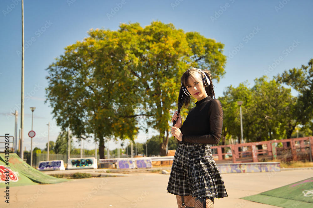 Young and beautiful girl with heterochromia and punk style with white headphones holding her pigtails with one hand looking at the camera.