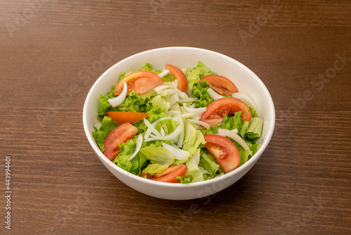 garden salad with chopped tomato, lettuce and crispy white onion in a simple white bowl and wooden table