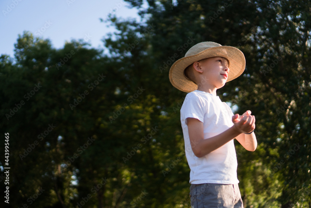 A cute boy in a hat and white shirt is playing around in nature.