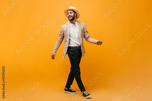 Man in hat and stylish outfit moving on orange background