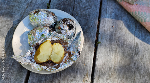 Potatoes cooked over a fire in hot coals. Food, vegetables in foil by the campfire on a picnic.  Outdoor food, evening dinner.