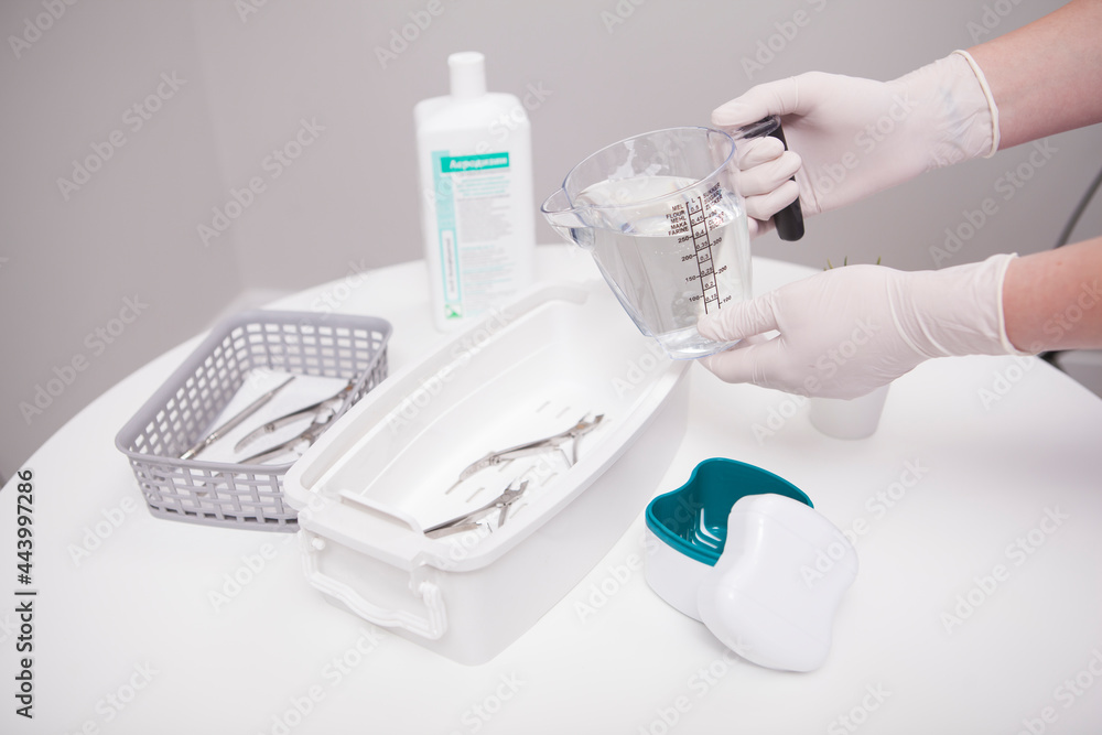 Manicurist pouring liquid sterilizer into container with nail nippers Manicurist pouring liquid sterilizer into container with nail nippers