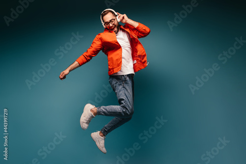 Active guy in headphones jumps on blue background