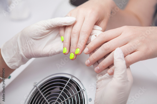 Cropped shot of manicurist examining nails of client after applying neon gel nail polish