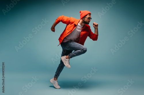 Young man in orange jacket fast running on isolated background