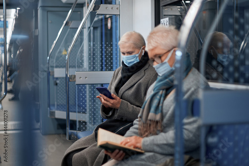 two mature passengers in protective masks sitting in a subway car.