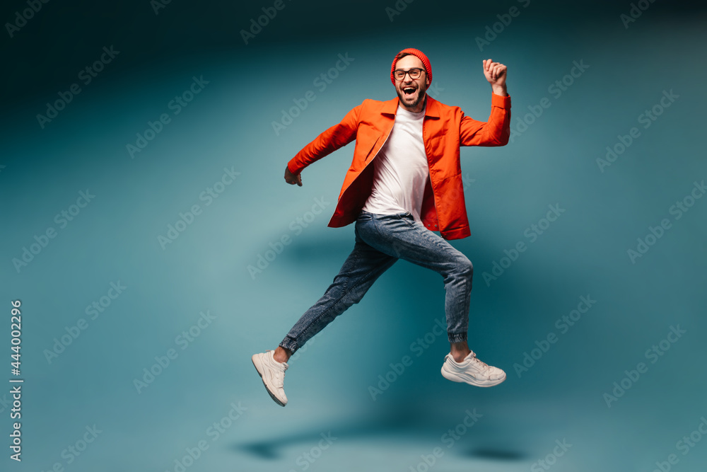 Happy man dressed in jeans and orange jacket runs on blue background