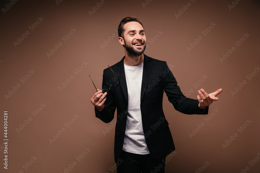 Charming man in suit posing with glasses on brown background Charming man in suit posing with glasses on brown background