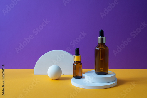 Amber glass dropper bottle with metallic lid on the white podium. Orange and purple background.. Container mockup with cosmetic oil or serum. Showcase for the presentation skincare products.