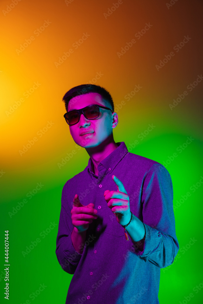 Handsome young man in sun glasses isolated on studio background in gradient green yellow neon light, colour filter. Concept of human emotions, facial expression. Handsome young man in sun glasses isolated on studio background in gradient green yellow neon light, colour filter. Concept of human emotions, facial expression.