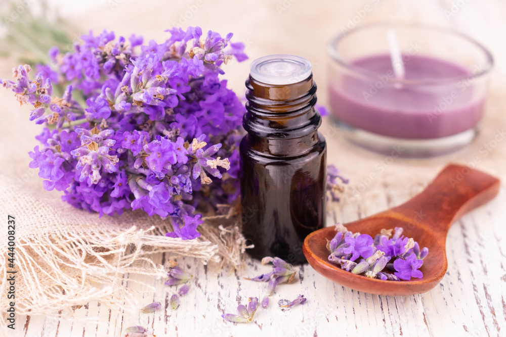 A bottle with lavender oil and delicate lavender flowers on a white background. A bottle with lavender oil and delicate lavender flowers on a white background.