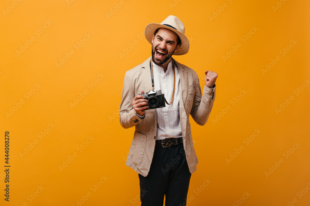Positive guy happily posing on orange background and holding retro camera Positive guy happily posing on orange background and holding retro camera