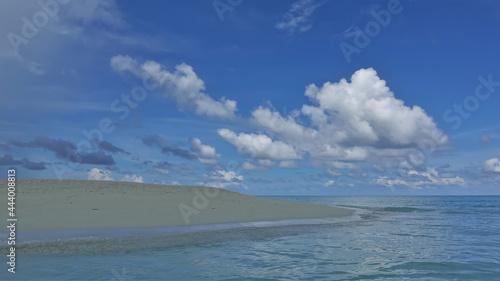 Calm blue and white Maldives landscape. The sandy promontory juts out into the turquoise ocean. There are picturesque cumulus clouds in the azure sky. No people