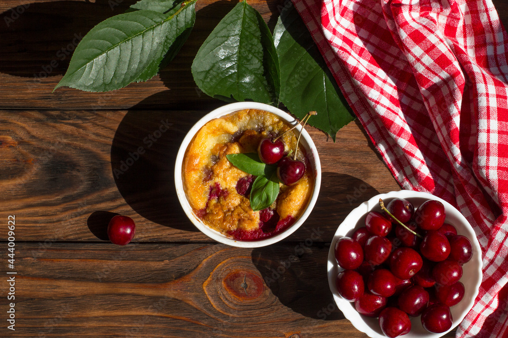 A portioned plate with clafoutis on a wooden background on a bright sunny day. Traditional French pie with cherry clafoutis. A portioned plate with clafoutis on a wooden background on a bright sunny day. Traditional French pie with cherry clafoutis.