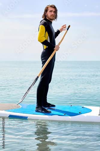 Young man in black wetsuit with paddle on sub board floats on water in ocean or sea, handsome caucasian man engaged in subsurfing alone. Healthy lifestyle concept, water sports. Copy space photo