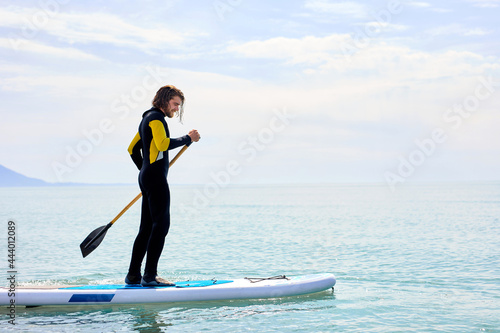 Side view on man in black wetsuit with paddle on sub board floats on water in ocean or sea, handsome caucasian man engaged in subsurfing alone. Healthy lifestyle concept, water sports. Copy space