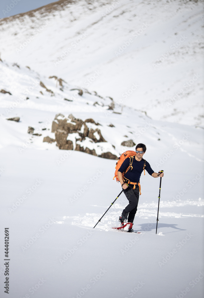 Winter sports - young man walking with snowshoes in high mountains covered with lots of snow (selective focus on the mountain in the background) Winter sports - young man walking with snowshoes in high mountains covered with lots of snow (selective focus on the mountain in the background)