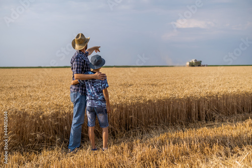 Farmers are standing in their wheat field while the harvesting is taking place. Father is teaching his son about agriculture.