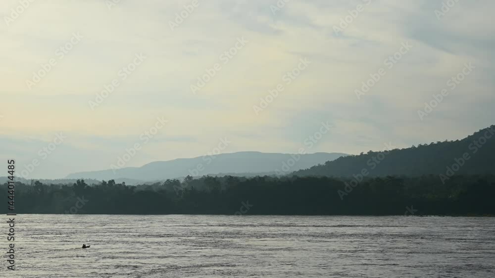 A boat crossing the Mekong river in a diagonal direction towards Laos from Thailand with a background of forest and hills. A boat crossing the Mekong river in a diagonal direction towards Laos from Thailand with a background of forest and hills.