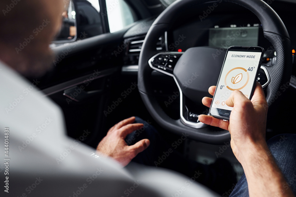 Sits in the car. Close up view of man's hand that holds phone with labels and icons. Conception of remote control Sits in the car. Close up view of man's hand that holds phone with labels and icons. Conception of remote control