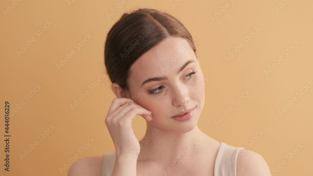 A beautiful woman is posing while showing secret gesture to the camera standing isolated over beige wall in the studio A beautiful woman is posing while showing secret gesture to the camera standing isolated over beige wall in the studio