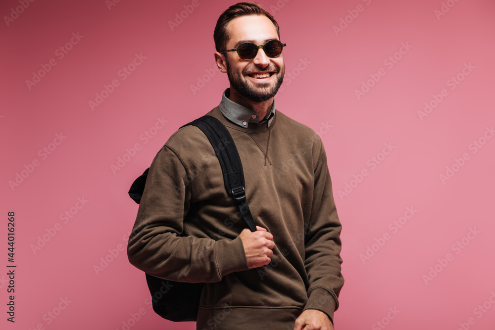 Fototapeta premium Handsome man in sunglasses and brown sweater holding backpack