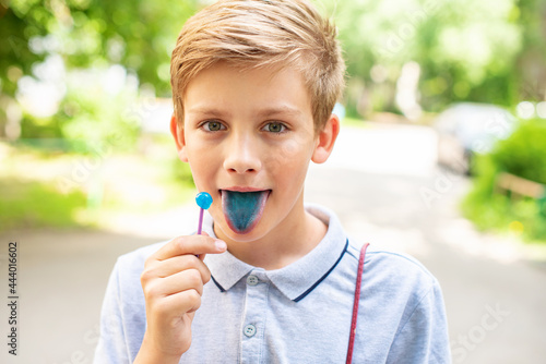 Foto Teen blonde boy licking lollypops and showing colored blue tongue