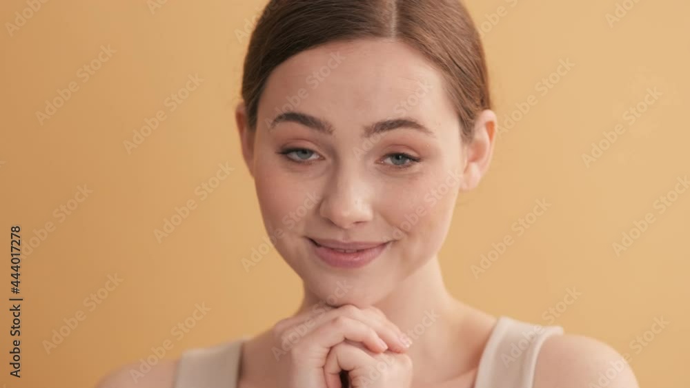 A pleased woman is looking at something nice and cute standing isolated over beige wall in the studio A pleased woman is looking at something nice and cute standing isolated over beige wall in the studio