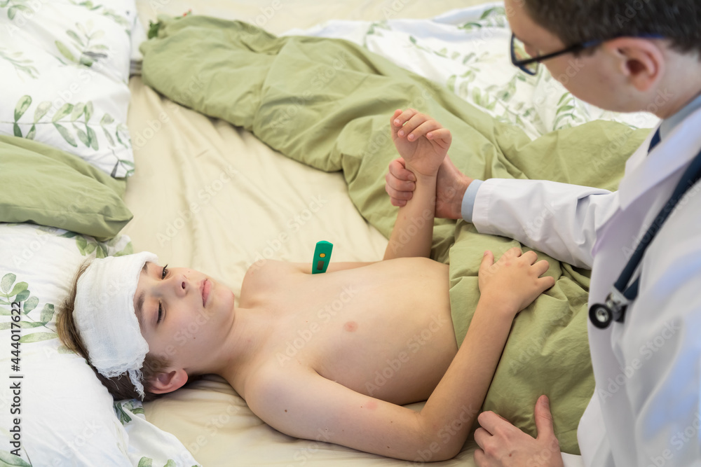 The doctor examines the patient with the temperature, measured the body  temperature. Cooling wet bandage on the teen's head. A boy lies in bed  Stock-Foto | Adobe Stock