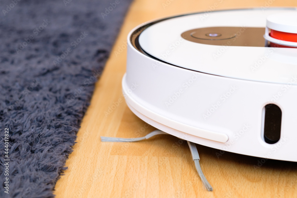 Robot vacuum cleaner performs cleaning of the wooden floor near the carpet. Housekeeping smart technology Robot vacuum cleaner performs cleaning of the wooden floor near the carpet. Housekeeping smart technology