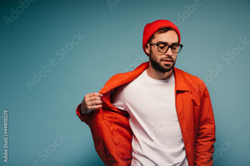 Man in glasses and hap puts off orange jacket