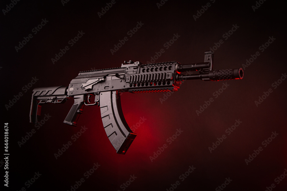A pneumatic copy of a Russian machine gun. Modern airsoft weapons. Dark background with red illumination. A pneumatic copy of a Russian machine gun. Modern airsoft weapons. Dark background with red illumination.