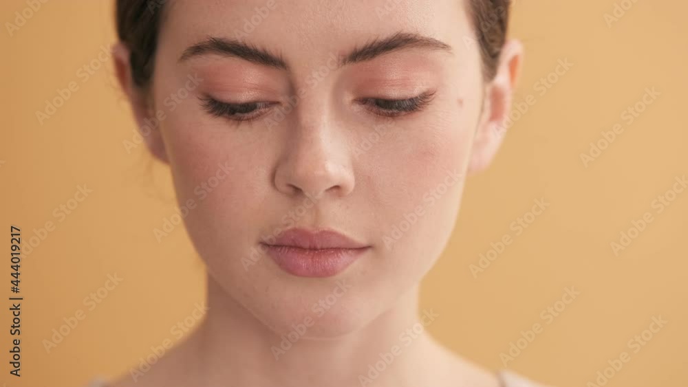 A close-up view of a beautiful woman is looking to the camera standing isolated over beige wall in the studio A close-up view of a beautiful woman is looking to the camera standing isolated over beige wall in the studio