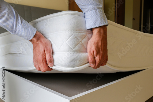 New bed delivery and assembly service concept. Cropped shot of male worker's hands in process of laying the orthopedic foam mattress on carcass in customer's bedroom. Close up, copy space, background. photo