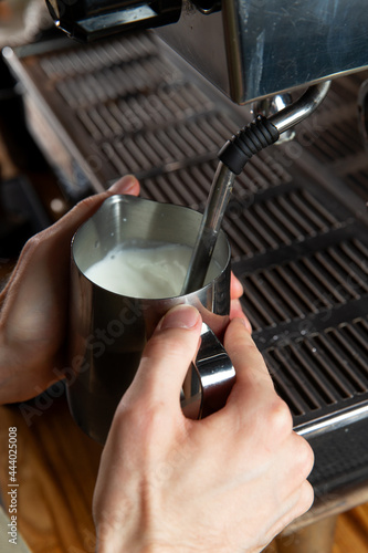 The barista pours milk into the pitcher.
