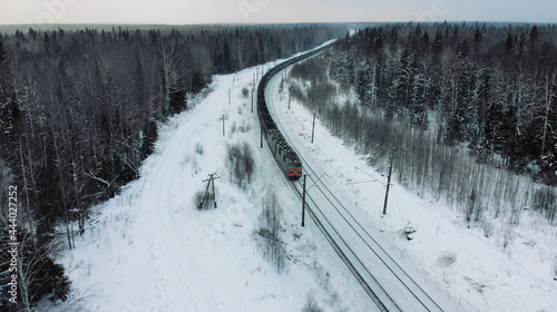 AERIAL. Winter shot of huge train with coal inside. Snow falling down in winter forest.