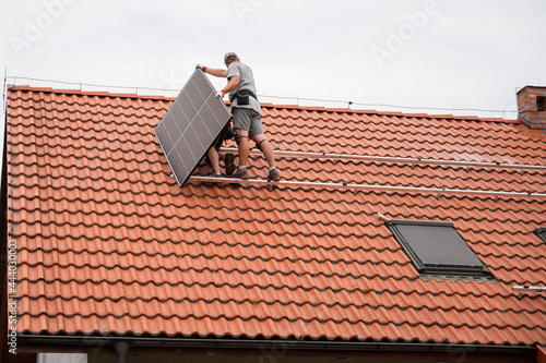 Two engineers on the house roof assemble photovoltaic panel.