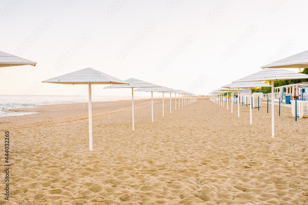 Empty sandy beach alond the sea with white umbrellas. Beach without tourists due to pandemic