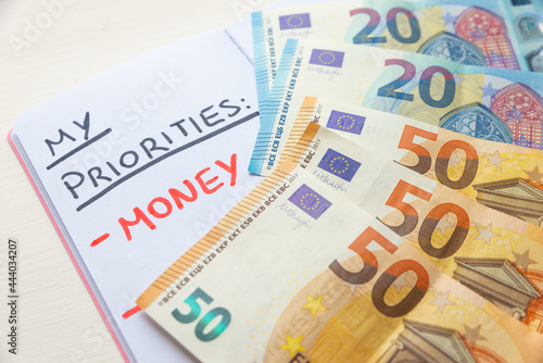 Blank diary page, with "Priorities" text in black ink; and text "Money" in red ink, with Euro banknotes beside it. Wealth and purpose in life. 