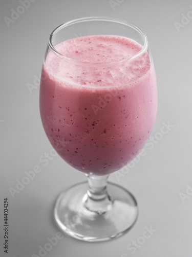 Delicious cold milkshake with cherries in glass on gray background