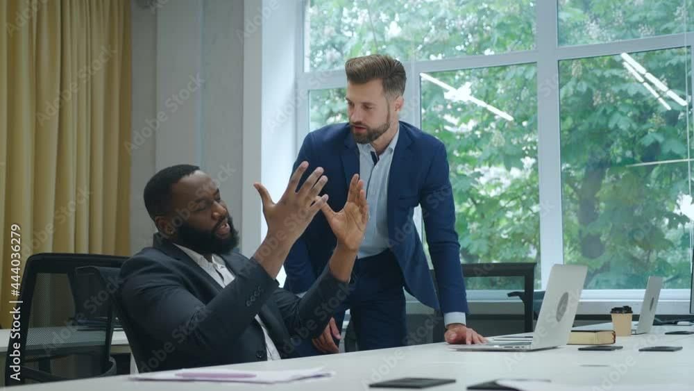 Two angry businessmen arguing having conflict confrontation while working at laptop computer at office. Two aggressive colleagues in suits arguing and shouting in office at each other. Two angry businessmen arguing having conflict confrontation while working at laptop computer at office. Two aggressive colleagues in suits arguing and shouting in office at each other.