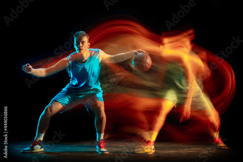 Young caucasian male basketball player playing basketball isolated over dark studio background in mixed light. Concept of healthy lifestyle  professional sport  hobby.