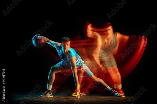 Professional male basketball player in blue uniform playing basketball isolated over dark studio background in mixed light. Concept of healthy lifestyle, professional sport, hobby.