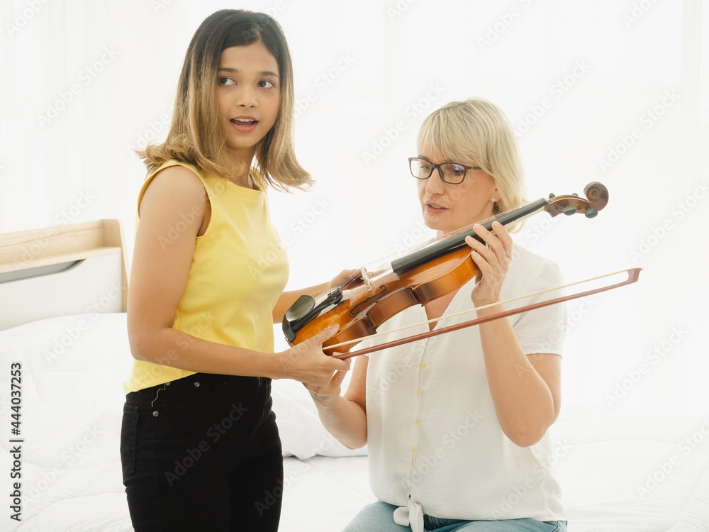 An adopted Asian teenage daughter is teaching her Caucasian mother-in-law how to play Violin during the holidays in the living room.. An adopted Asian teenage daughter is teaching her Caucasian mother-in-law how to play Violin during the holidays in the living room..
