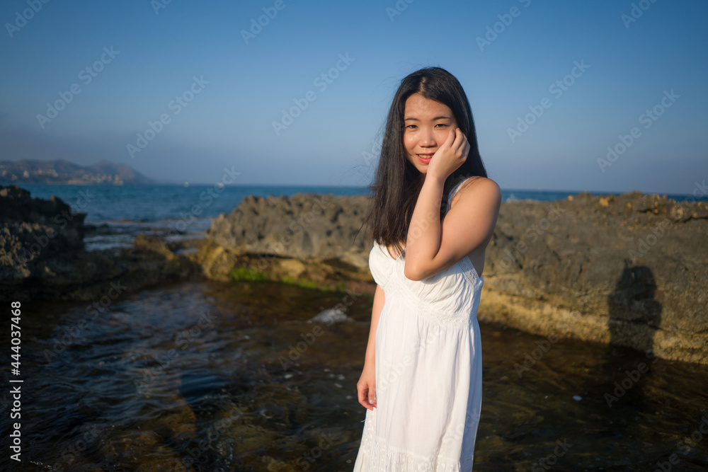 summer lifestyle portrait of young beautiful and happy Asian woman at the beach - Attractive Korean girl by the sea enjoying holidays trip on rock cliff with ocean view