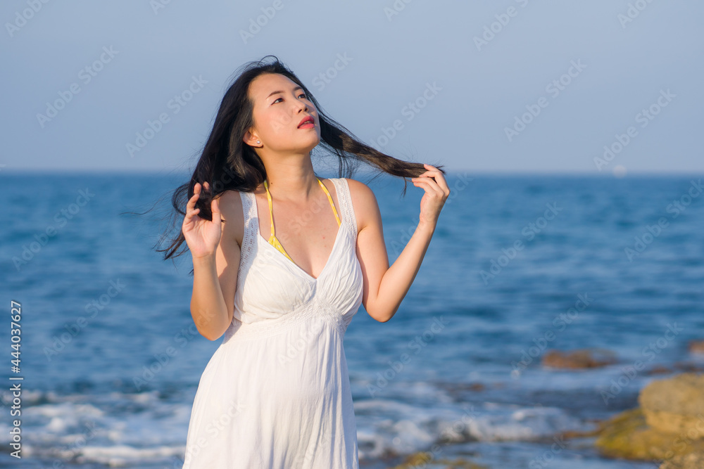 summer lifestyle portrait of young beautiful and happy Asian woman at the beach - Attractive Korean girl by the sea enjoying holidays trip on rock cliff with ocean view