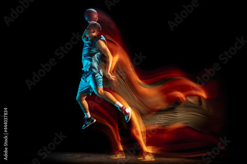 Young caucasian man, male basketball player playing basketball isolated over dark studio background in mixed light. Concept of healthy lifestyle, professional sport, hobby.