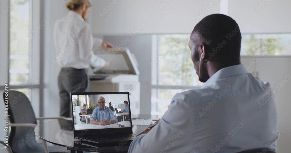 Back view of african employee sitting at desk in office having video chat with boss on laptop Back view of african employee sitting at desk in office having video chat with boss on laptop
