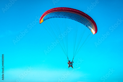 Doubles paragliding against a clear blue sky. A multi-colored papaplan flies in the clear sky closeup.